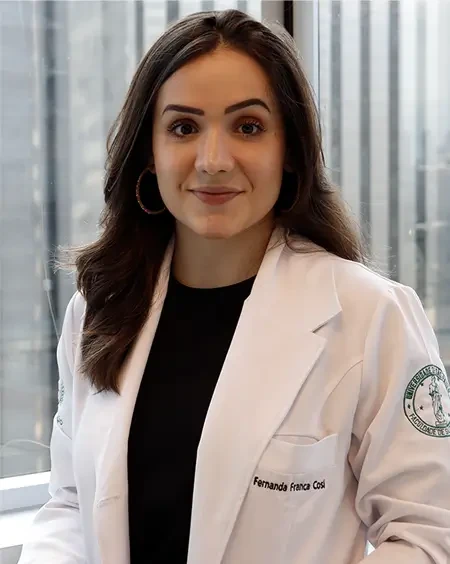 Fernanda Cosi de jaleco branco, sorrindo, com o skyline de São Paulo ao fundo